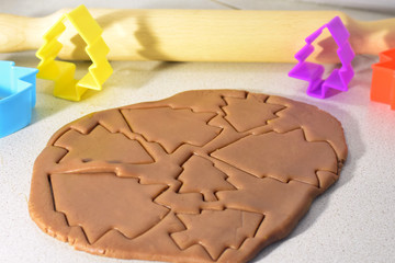 Christmas ginger dough with cutting new year tree cookies for holiday and blurred colorful plastic forms with wooden rolling pin on background