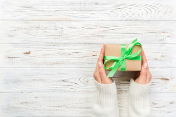 Woman hands give wrapped valentine or other holiday handmade present in paper with green ribbon. Present box, decoration of gift on wooden table, top view with copy space