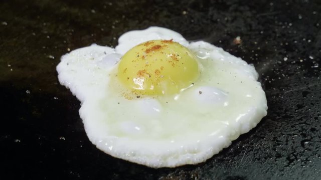 Close-up shot of broken egg being fried on hot oiled cast iron grill. 4K