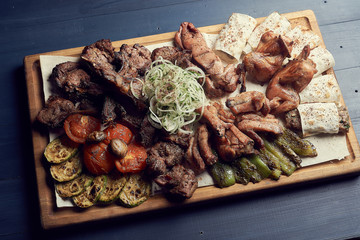 Grilled meat and vegetables with fresh onion on wooden plate