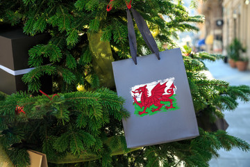 Wales flag printed on a Christmas shopping bag. Close up of a shopping bag as a decoration on a Xmas tree on a street. New Year or Christmas shopping, local market sale and deals concept. 