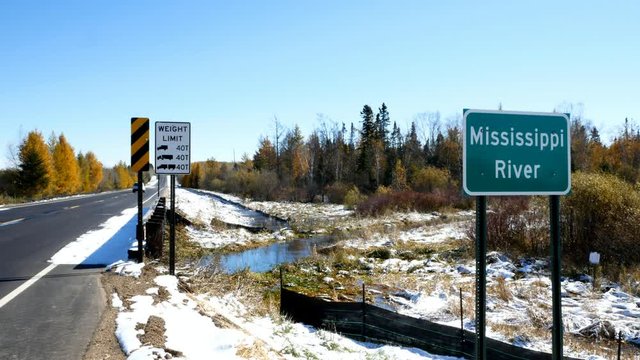 Mississippi River flowing north near its source at Itasca State Park in Minnesota. A car drives by this sign at the fifth highway bridge over the Mississippi River after an early autumn snowfall.