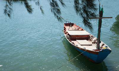 Obraz premium fisherman fishing boat anchored at pier under pine tree with natural blue green seawater background. marine vessel, occupational tool and equipment, transportation, agriculture or fishery concept.