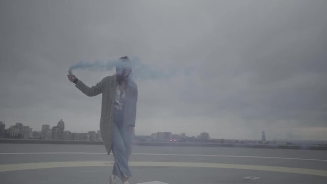 Young woman with smoke bomb over city background. Slow motion, s-log, ungraded