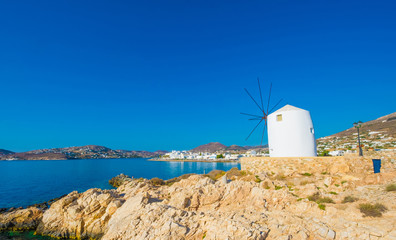 Fototapeta na wymiar Old white windmill on the cliff in front of water and beautiful blue sky at sunny day, Paros, Greece