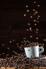 Roasted coffee beans falling down on white cup on wooden table