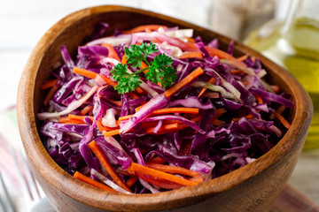 Fresh coleslaw salad with red and white cabbage and carrots in bowl on white wooden background. Selective focus.