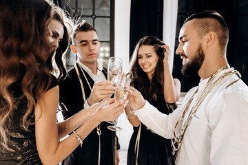 Сompany of beautiful young girls and guys dressed in stylish elegant clothes stand together and clink glasses with champagne. Party time
