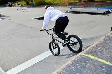 Full length back view portrait of modern young man doing stunts on bmx bike going down ramp in skateboarding park, copy space