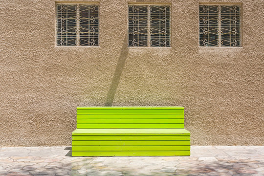 A bright green bench placed under three windows in the old quarter of Dubai