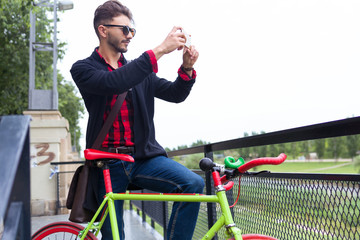 Stylish man in sunglasses with bike making photo via mobile phon