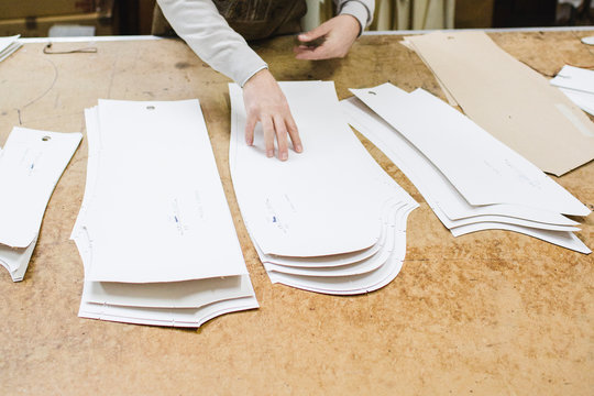 Tailor arranges on the desk the paper patterns in his atelier