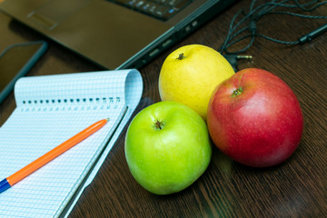 Write ideas into a notebook with a pen, laptop, headphones and apples for healthy eating