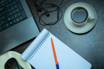 a clean notebook on the desktop, next to the laptop, a cup of coffee, headphones. A place to create ideas