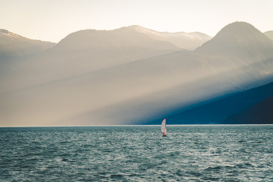 Small sailboat on the water in front of giant beams of light in the mountains