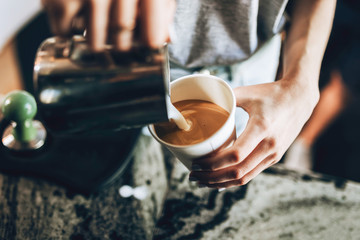 A young good looking blonde,wearing casual style,holds a glass and milk frother in a cozy coffee shop.