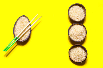 Rice in organic coconut bowl with chopsticks on geometric paper background. Yellow  trendy color, close up,copy space