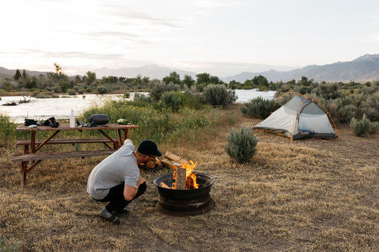 Young adult male starts fire at campsite next to river