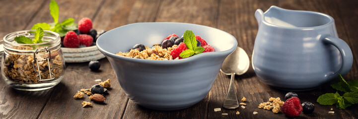 Oat granola with berries and yoghurt in blue bowl on dark old wooden background. Healthy breakfast...