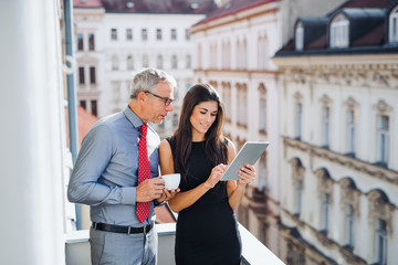 Man and woman business partners with tablet standing on a terrace in city, talking.