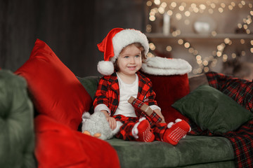 Christmas cute toddler girl in Santa hat holding a a gift box. Family holiday concept.