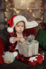 Christmas cute toddler girl in Santa hat holding a a gift box. Family holiday concept.