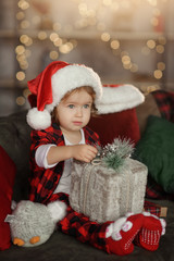 Fototapeta na wymiar Christmas cute toddler girl in Santa hat holding a a gift box. Family holiday concept.