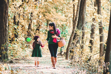 A young mother with a toddler daughter walking in forest in autumn nature.