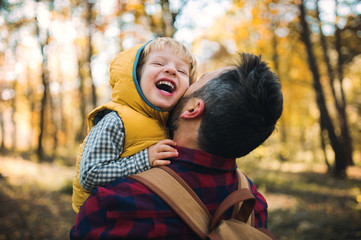 A mature father holding a toddler son in an autumn forest, having fun.