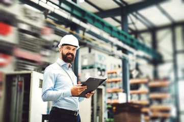 A portrait of an industrial man engineer with clipboard standing in a factory.