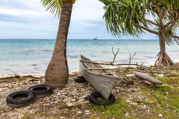 Traditional Polynesian outrigger canoe atop old tires on a rocky shore of atoll lagoon under...