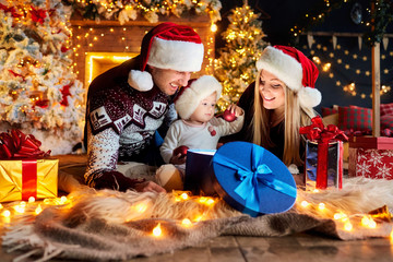 Happy family with a baby in a Santa Claus hat in a Christmas room in Christmas day.