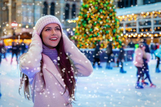 Junge Frau in winterlicher Kleidung auf einem Weihnachtsmarkt freut sich über den Schneefall