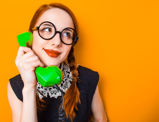 surprised young girl in glasses with two pigtails holding handset on yellow background