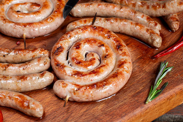 Grilled sausage ring on wooden board. There is a sprig of rosemary.