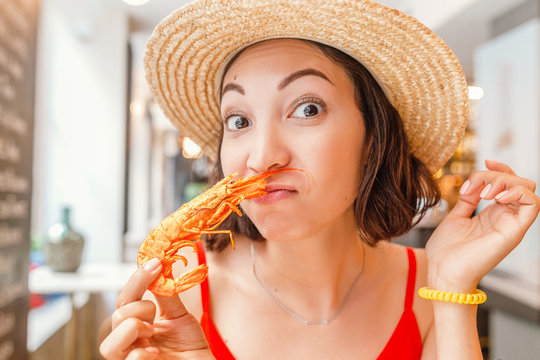 Happy Asian woman in hat eating local Spanish cuisine grilled seafood