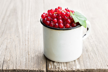 Fresh red currant in old white mug on wooden table