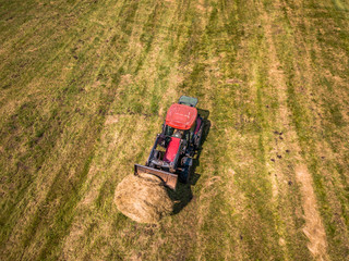 Obraz premium Aerial Drone Photo of Farmer Harvesting Hay Rolls in the Wheat Field with a Red Tractor
