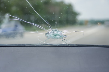 The broken windshield of the car from flying stone. The hole in the glass, chips and debris, cracks in strips. The glass reflects the sky with clouds.