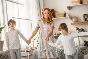 blonde caucasian baby two years old in brunette woman mother arms breastfeeding sitting on bed white clothes in bedroom next to window indoor. Woman is back.