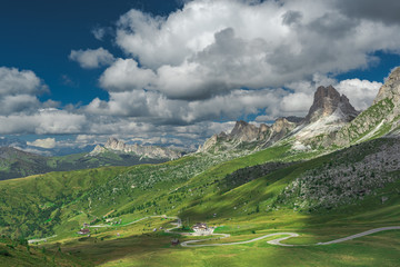 Green grass and blue sky with clouds around high mountains, Dolomites in Italy.