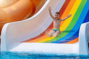 Little boy with hands up sliding into water in aqua park