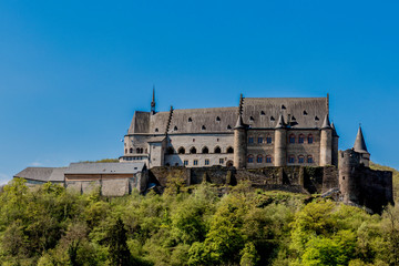 Fototapeta na wymiar Aerial and side view of the castle of Vianden surrounded by lush green trees, blue sky in the background, it was built in Romanesque style between the 11th and 14th centuries, sunny day in Luxembourg