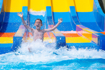 Cheerful boy splashing water on water slide at aqua park