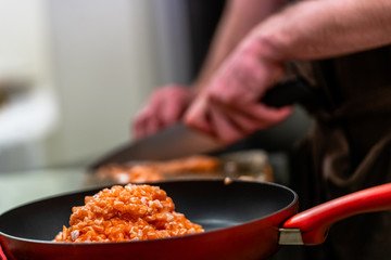 Red Pan with Pile of Cutted Salmon Pieces in the Foreground, Male Chef Cutting Fresh Salmon on the Wooden Board in the Background