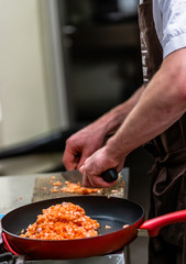 Red Pan with Pile of Cutted Salmon Pieces in the Foreground, Male Chef Cutting Fresh Salmon on the Wooden Board in the Background