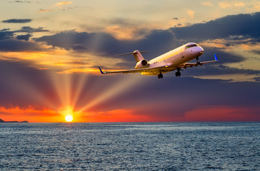 private business jet plane flying over the sea at sunset, the sun's rays cut through the clouds