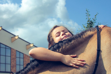 Girl hugging horse gold color. Blue sky , outside, farm near stables. Concept of spring and summer sports, care, good mood, horse trainings; equistrain club; hippotherapy; vacation and hobby