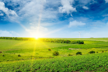 Hilly green field , sun rise and windmill on blue sky background.