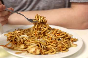 Unrecognizable person eating Chinese food, noodles with chicken and vegetables. Close-up, selective focus.
